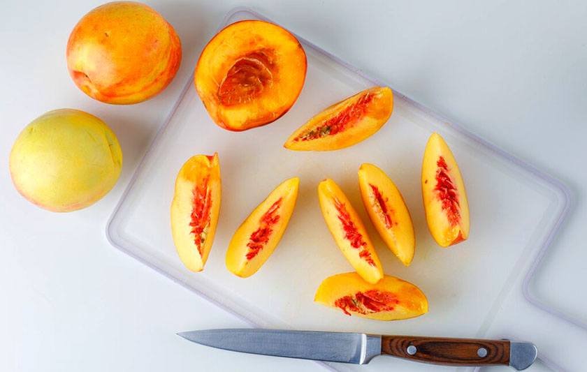 Peaches and cut pieces of them on a cutting board and a knife