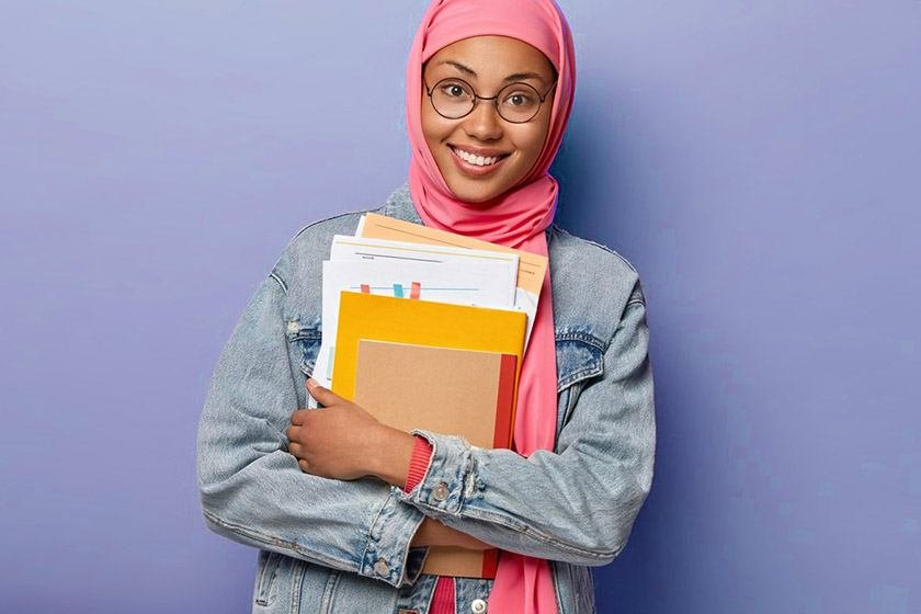 An Arabic girl with glasses holding a couple of books and documents