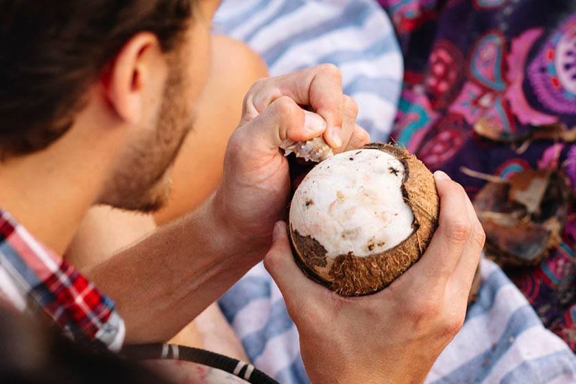 A man holds a coconut while removing the husk with a whelk