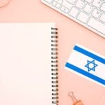 Israel flag next to an empty notebook, glasses, and keyboard which can be part of the best way to learn Herbrew