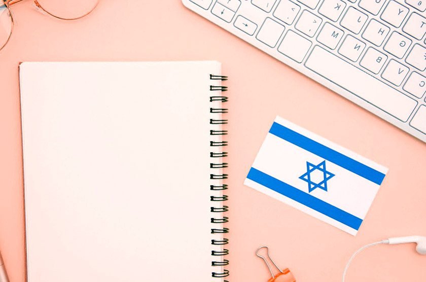 Israel flag next to an empty notebook, glasses, and keyboard which can be part of the best way to learn Herbrew