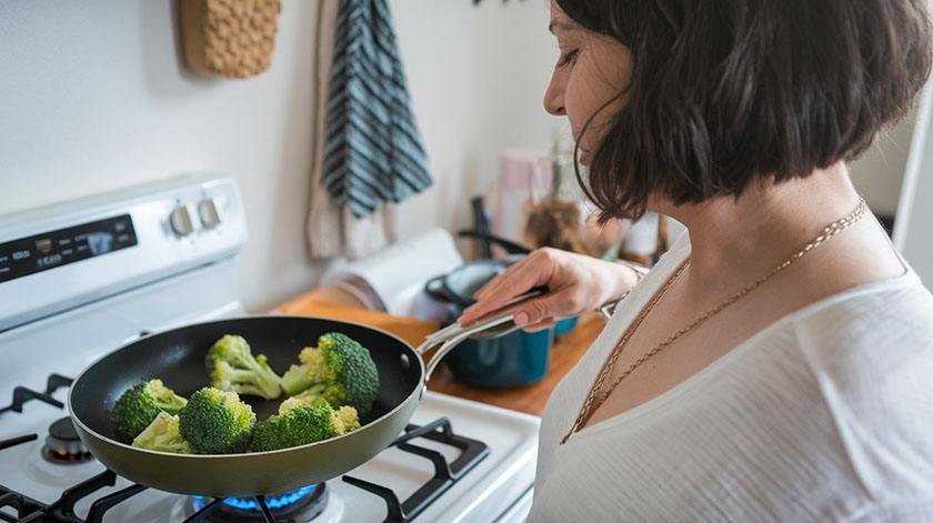 A woman cooks procolli on a pan over a stove