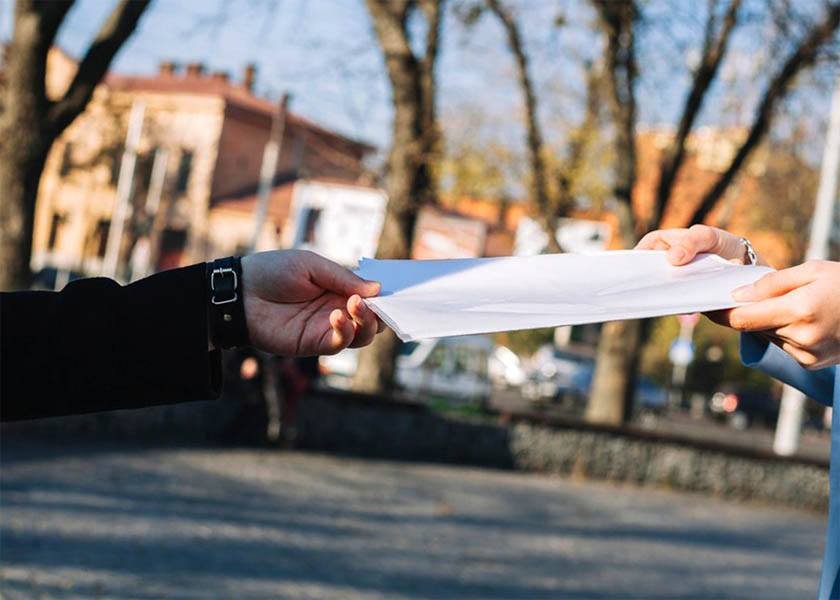 Two hands hand each other a document in the middle of the city