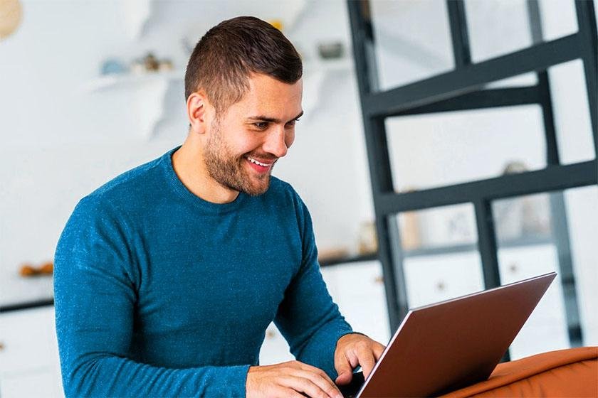 A man in a turquoise T-shirt runs an ad on his laptop