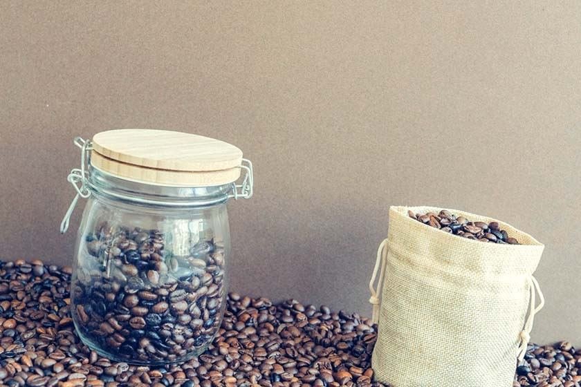 Coffee beans in a cloth bag, and next to them an airtight storage jar that again has coffee beans in it