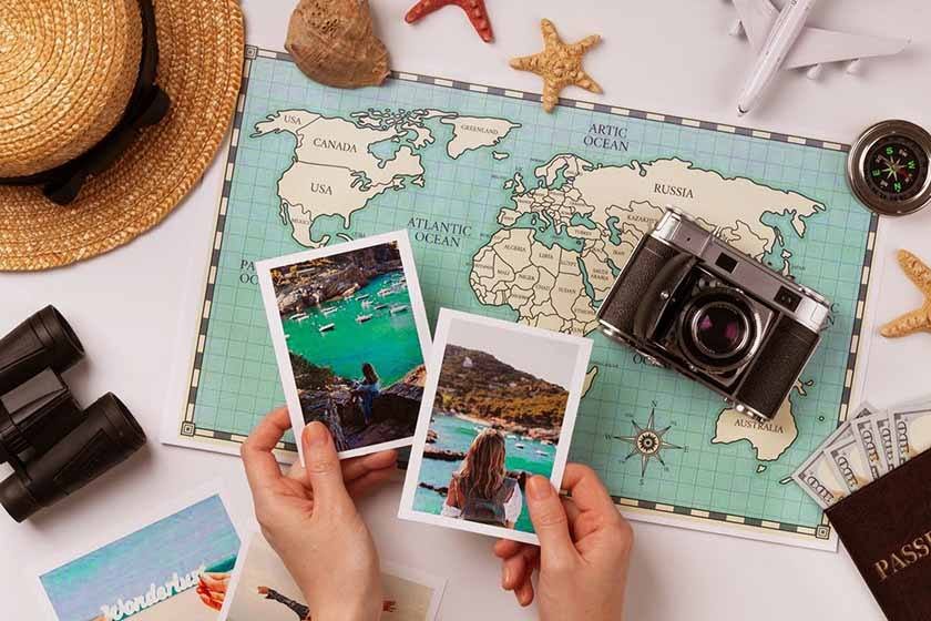 Pictures held by hands that are on a table on which there is a camera, binoculars, a world map and a hat, which can be part of the best way to travel europe