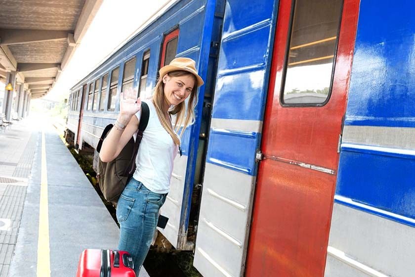 The smiling woman with a suitcase sitting in front of a train