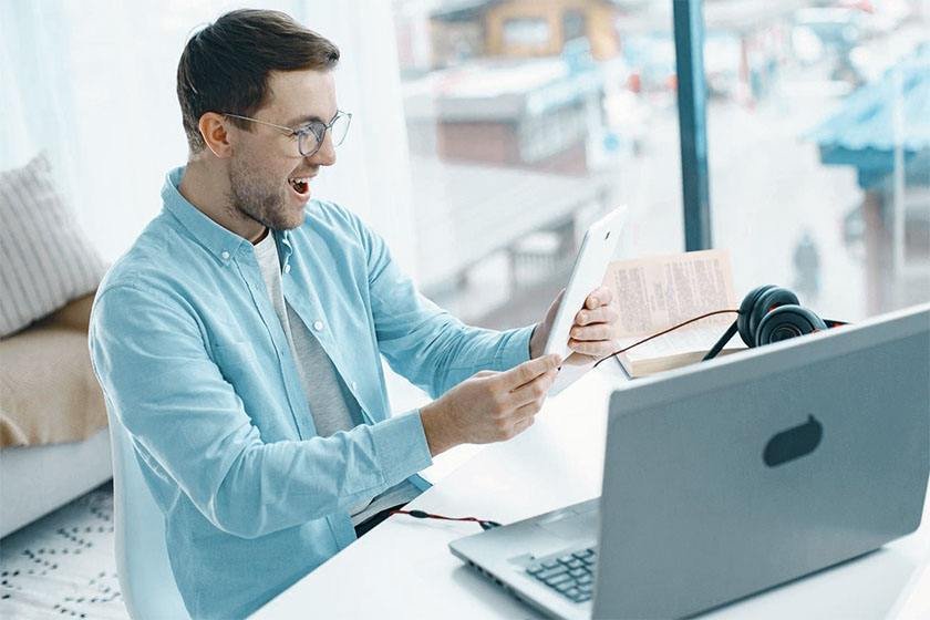 A room with a laptop, sofa and happy guy in the office holding his tablet 