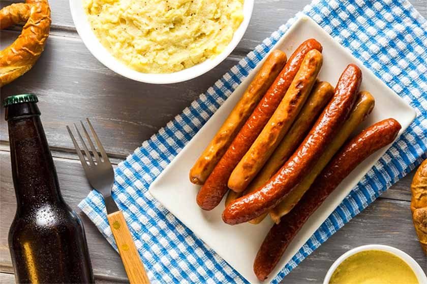 A table with brats, mashed potatoes, mustard, beer fork and bagel