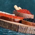 A wooden board on which there are slices of bread with caviar, which are part of the best way to eat caviar