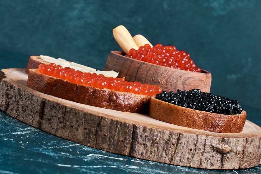 A wooden board on which there are slices of bread with caviar, which are part of the best way to eat caviar