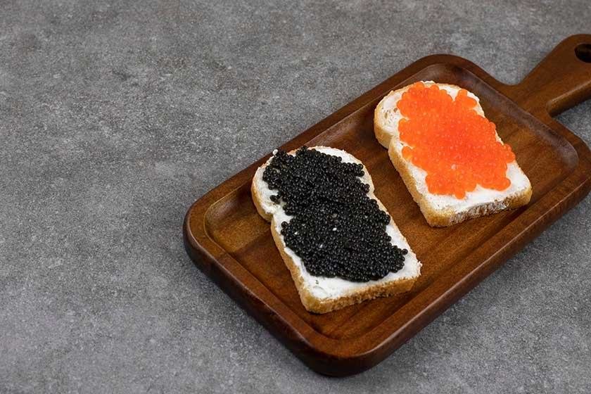 A wooden board on which there are slices of two types of caviar