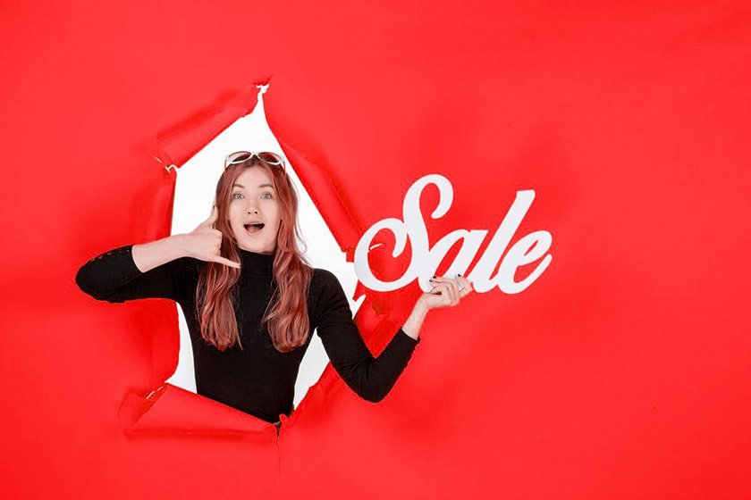 Amazed woman holding SALE sign on red background