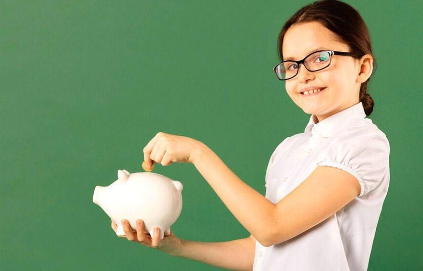 A girl with glasses drops a coin into a piggy bank