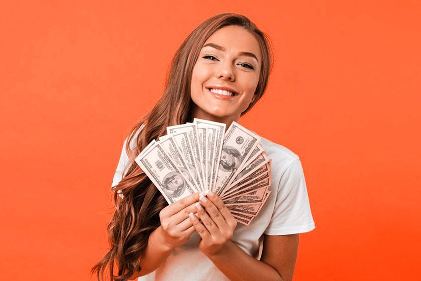 Smiling woman holding money on orange background