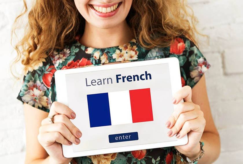 A woman is holding a paper with the French flag which can be the best way to learn French.