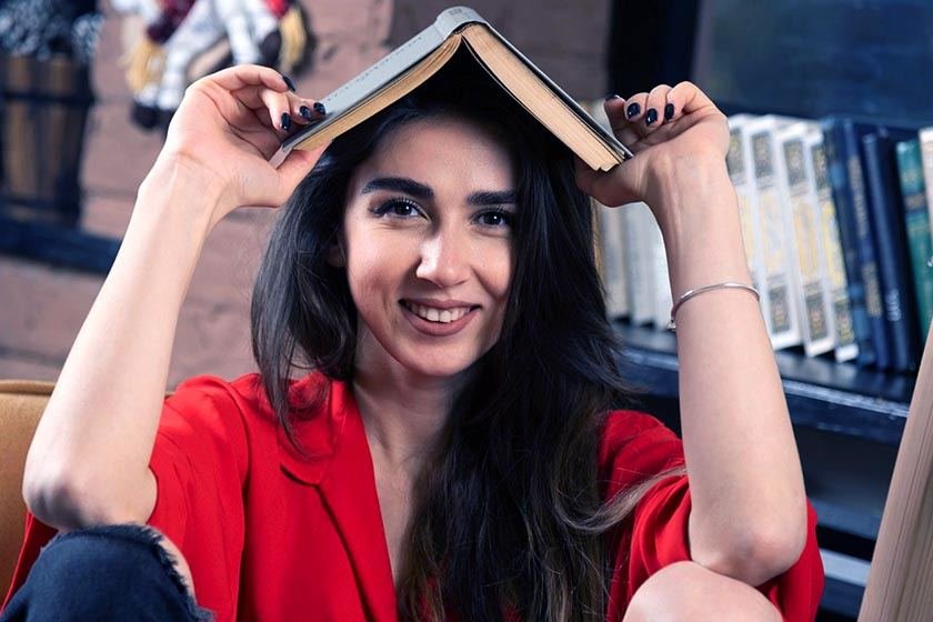 Smiling woman in red blouse holds an open book on her head