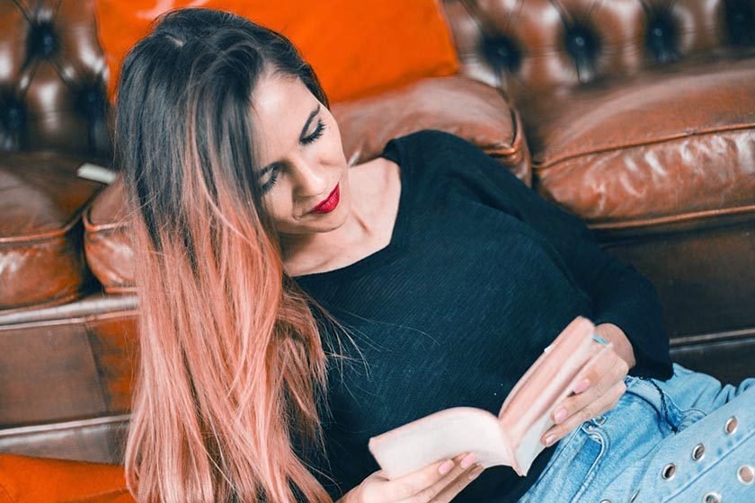 A beautiful woman is lying on the ground while reading in French near her sofa