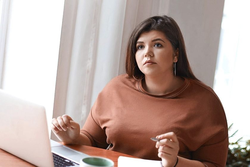 A woman looks in front of her while sitting and working on her laptop