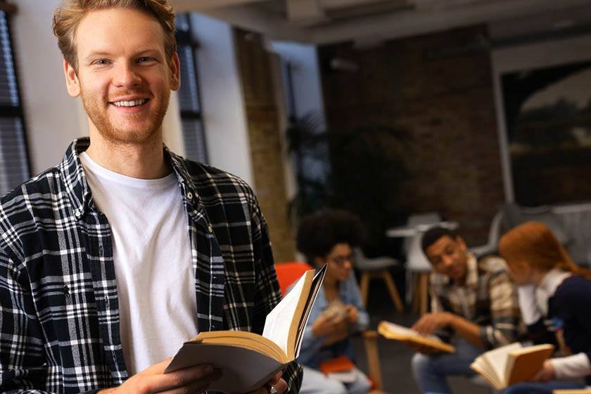 Smiling German man holding a book in a library