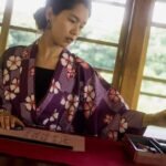 A Japanese woman in traditional clothes writes while using the best way to learn japanese