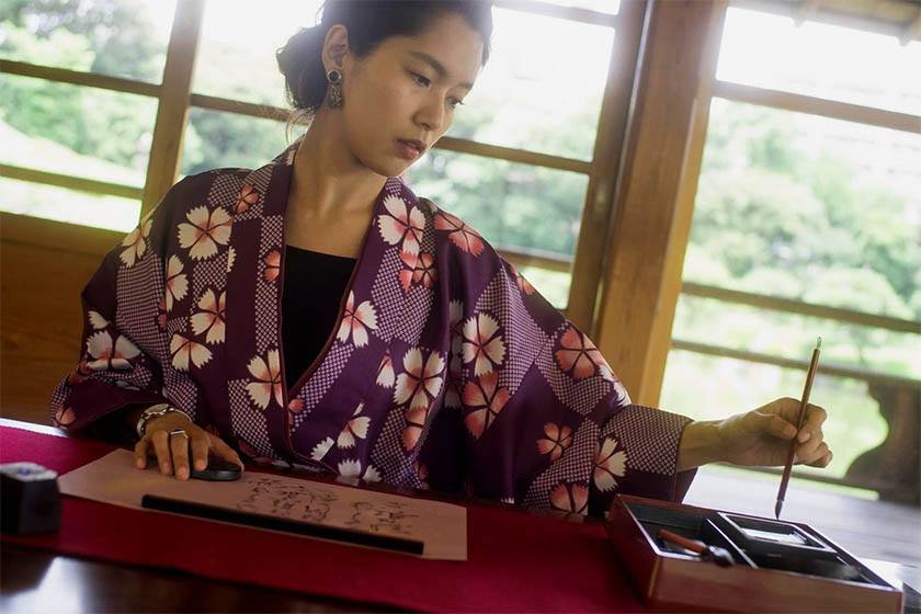 A Japanese woman in traditional clothes writes while using the best way to learn japanese