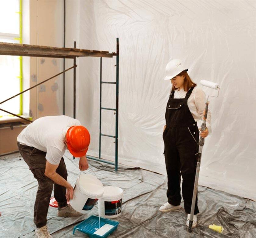 A man pours paint into a paint container while a woman sits and looks at him