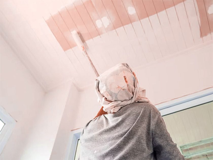 A woman with a towel on her head paints the ceiling white