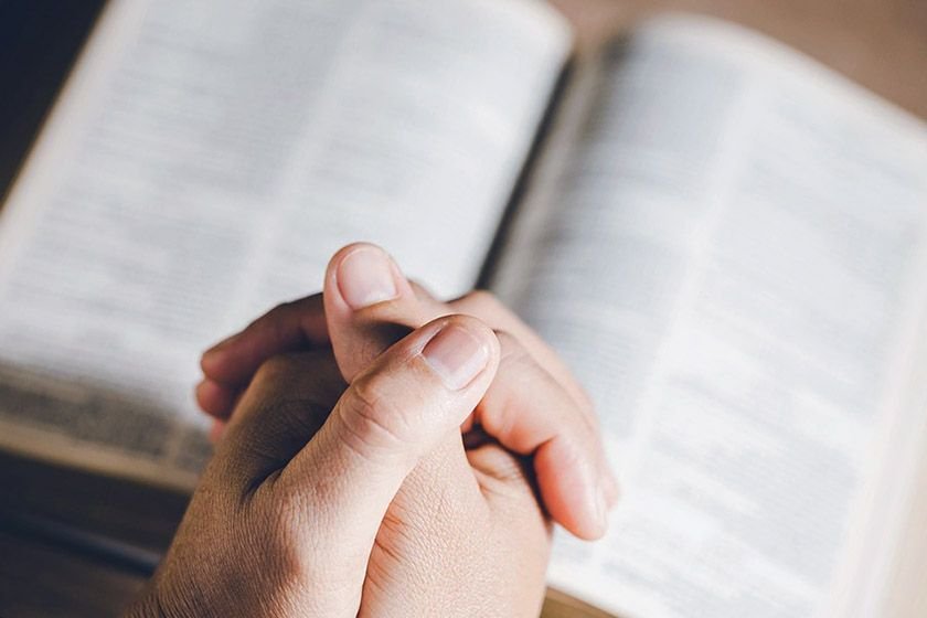 Close-up shot of fingers entwined with the bible in the background