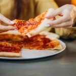 Hands held a pizza slice after using the best way to reheat pizza