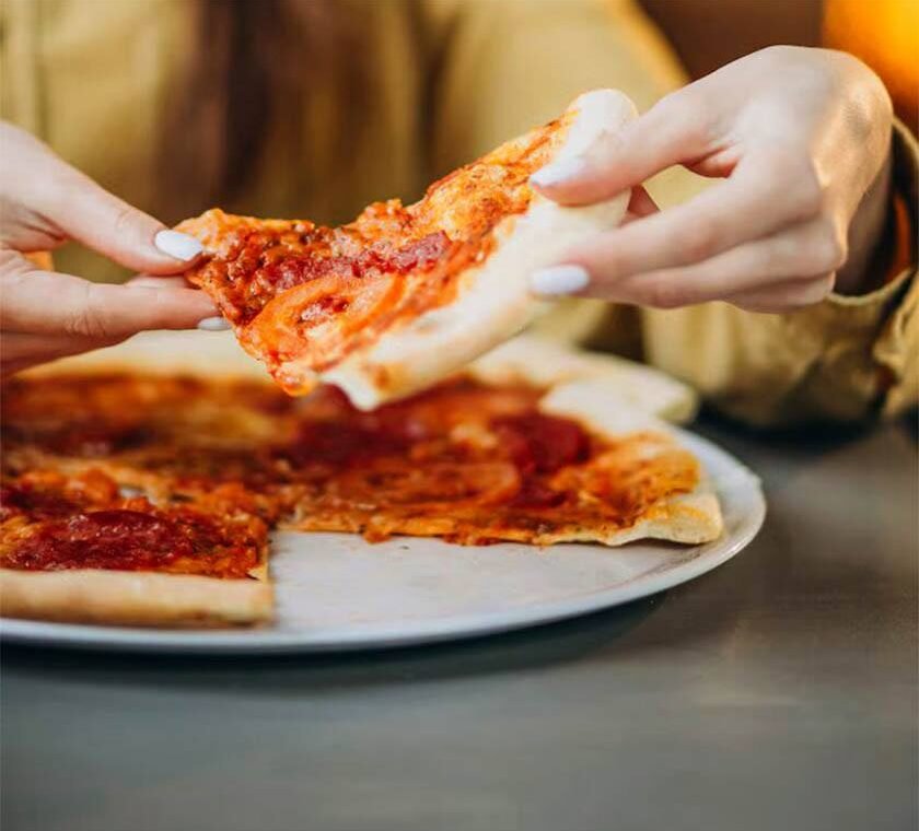 Hands held a pizza slice after using the best way to reheat pizza