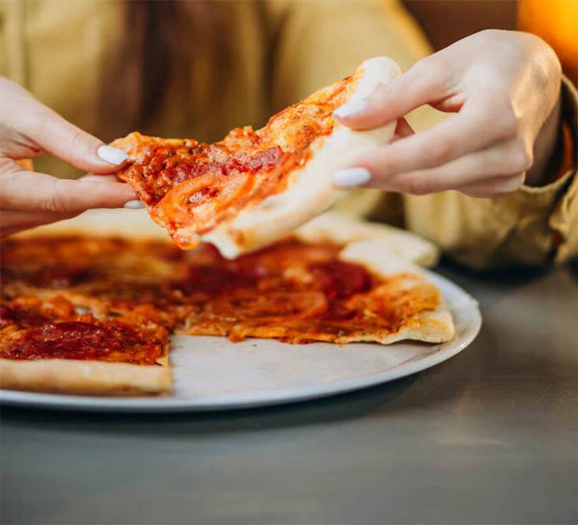 Hands held a pizza slice after using the best way to reheat pizza