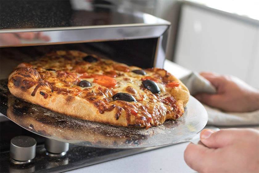 A man takes a pizza out of a small oven