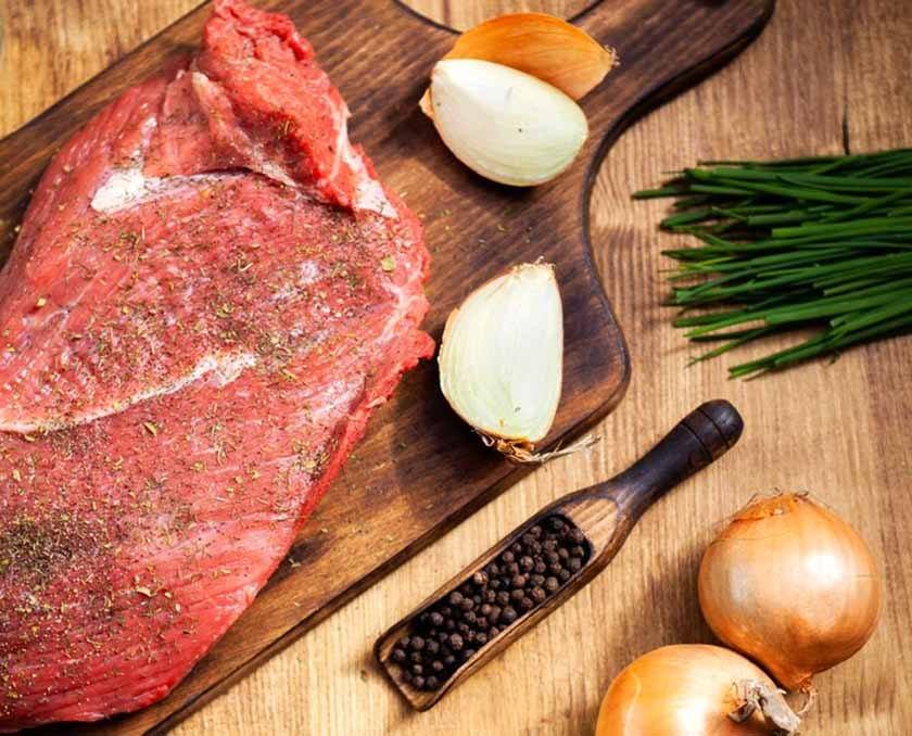 A kitchen board with onions, peppercorns, spring onions and seasoned steak, all of these products are part of the process for the best way to season steak