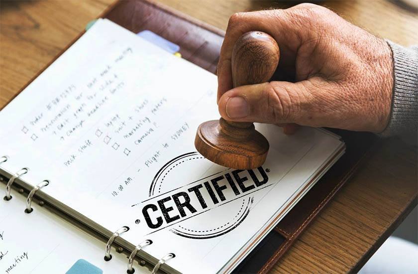 Photo of a hand holding a wooden stamp on a book that says certified 