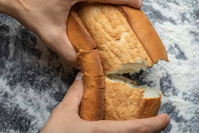 Hands break bread which can be part of the process of what it is the best way to store bread