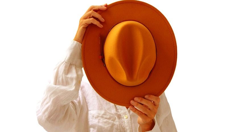 A man covering his face holding a hat by the brim