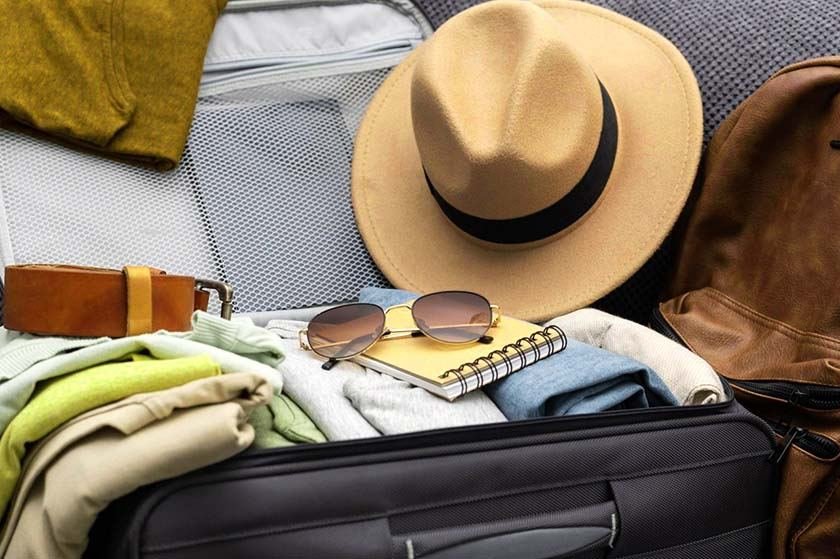 Open suitcase for travel with hat, glasses, clothes and belt