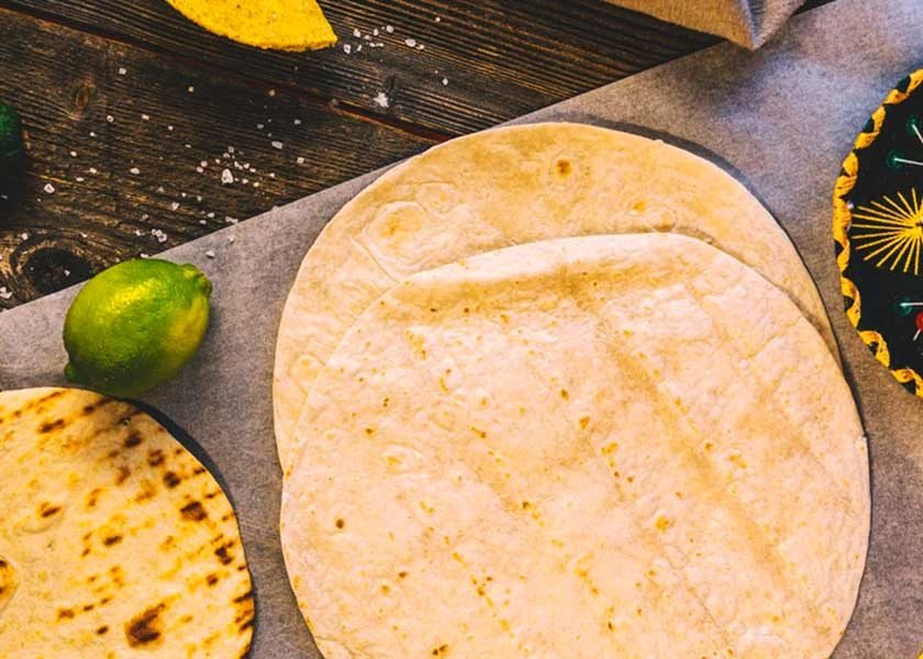 A table with a fresh corn tortilla, a toasted tortilla, and a lime