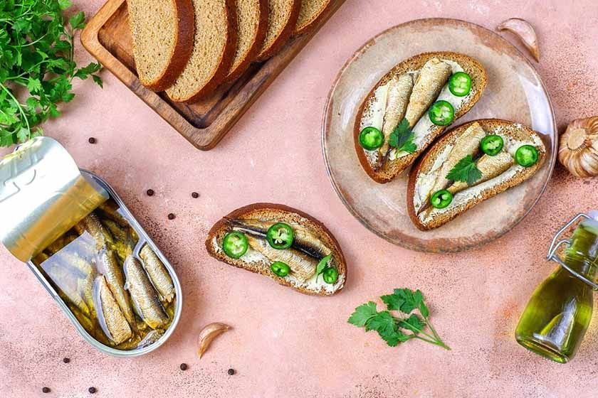 A slice of bread and another spread with cream cheese, peppers and sardines