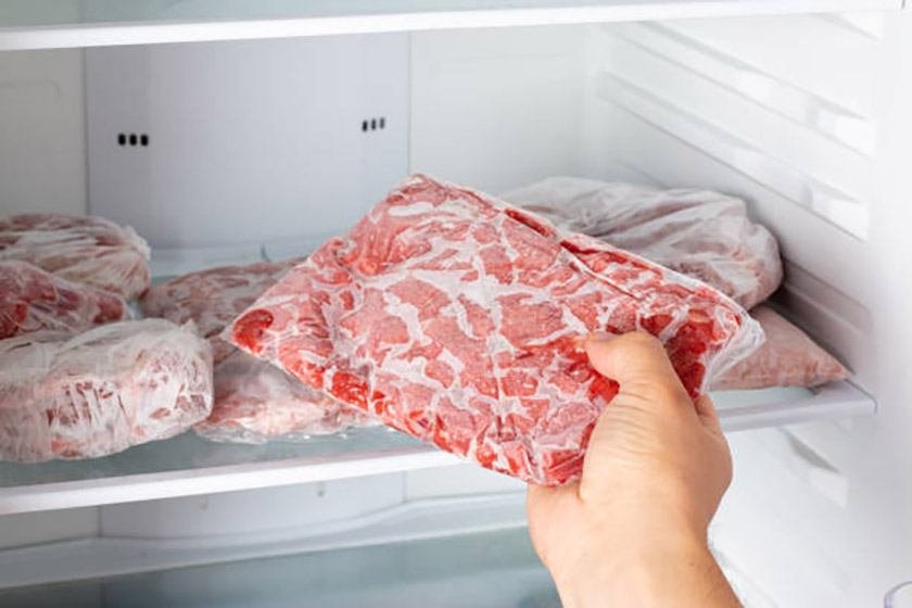 A hand puts a package of meat in the freezer