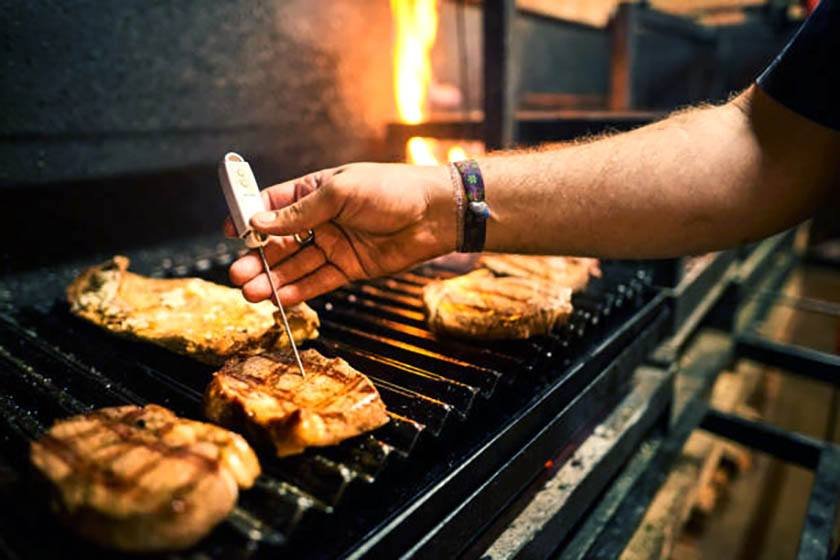 A hand holds a meat thermometer with which to measure the temperature of a grilled steak