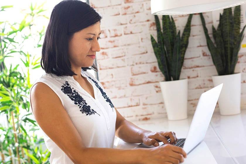 A woman sits at her desk and studies Portuguese on her laptop