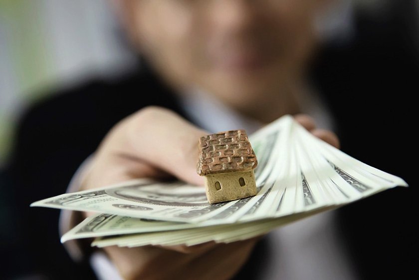 A man shows a sheet of money with a mini house on it