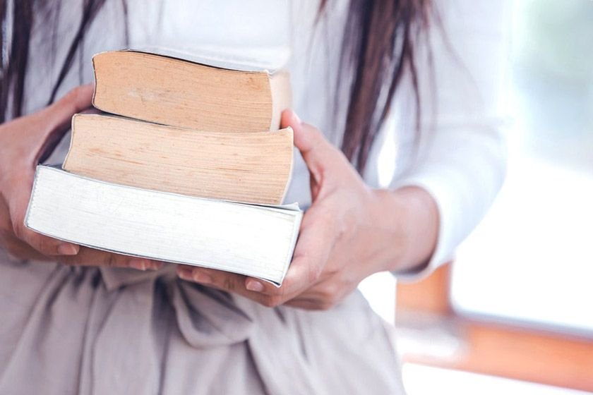 A woman holding 3 books in her hands