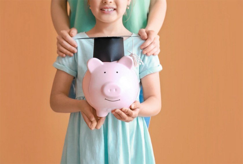 A kid holding a pig piggy bank with a student hat