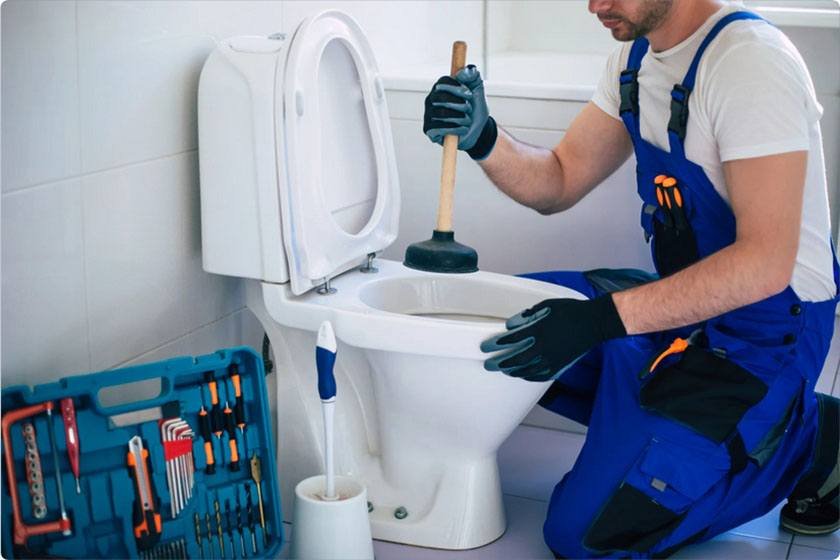 A worker performs the best way to unclog the toilet with a plunger