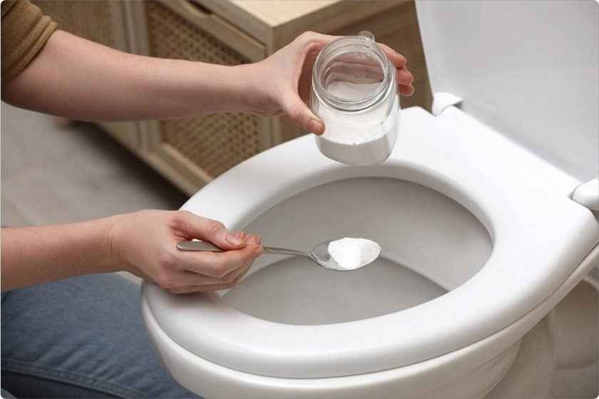 A woman puts baking soda into a toilet to unclog it 